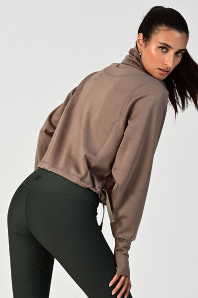 Back view of a woman posing & wearing the Rodeo khaki oversized half zip on a white background