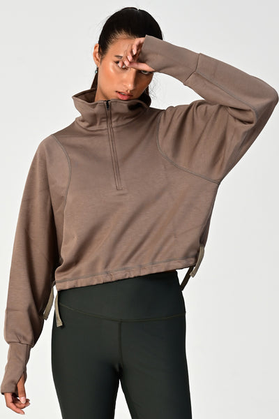 Front view of a woman posing & wearing the Rodeo khaki oversized half zip on a white background