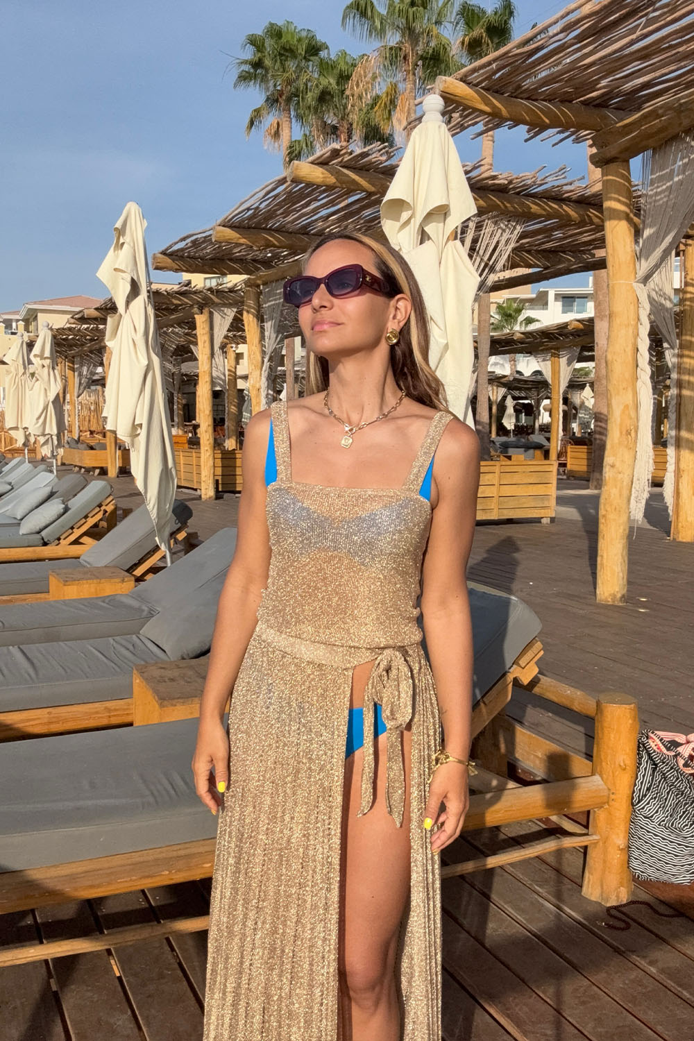 Woman in a beach setting wearing sunglasses and a long cover-up skirt.