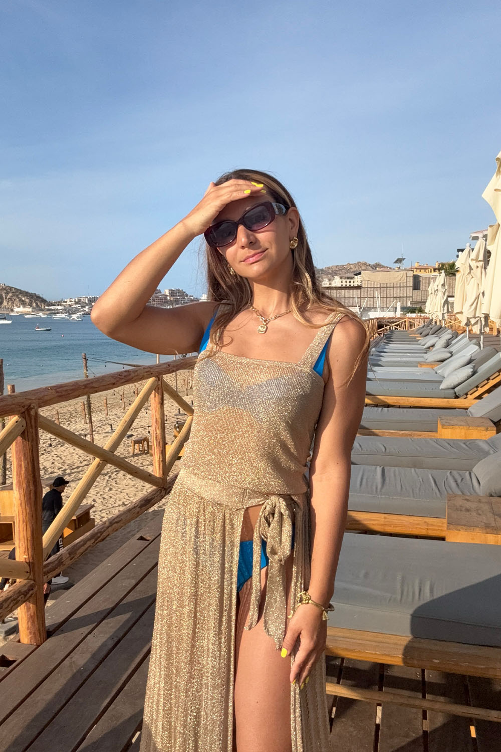 Woman in a blue bikini and gold cover-up standing on a deck with ocean view